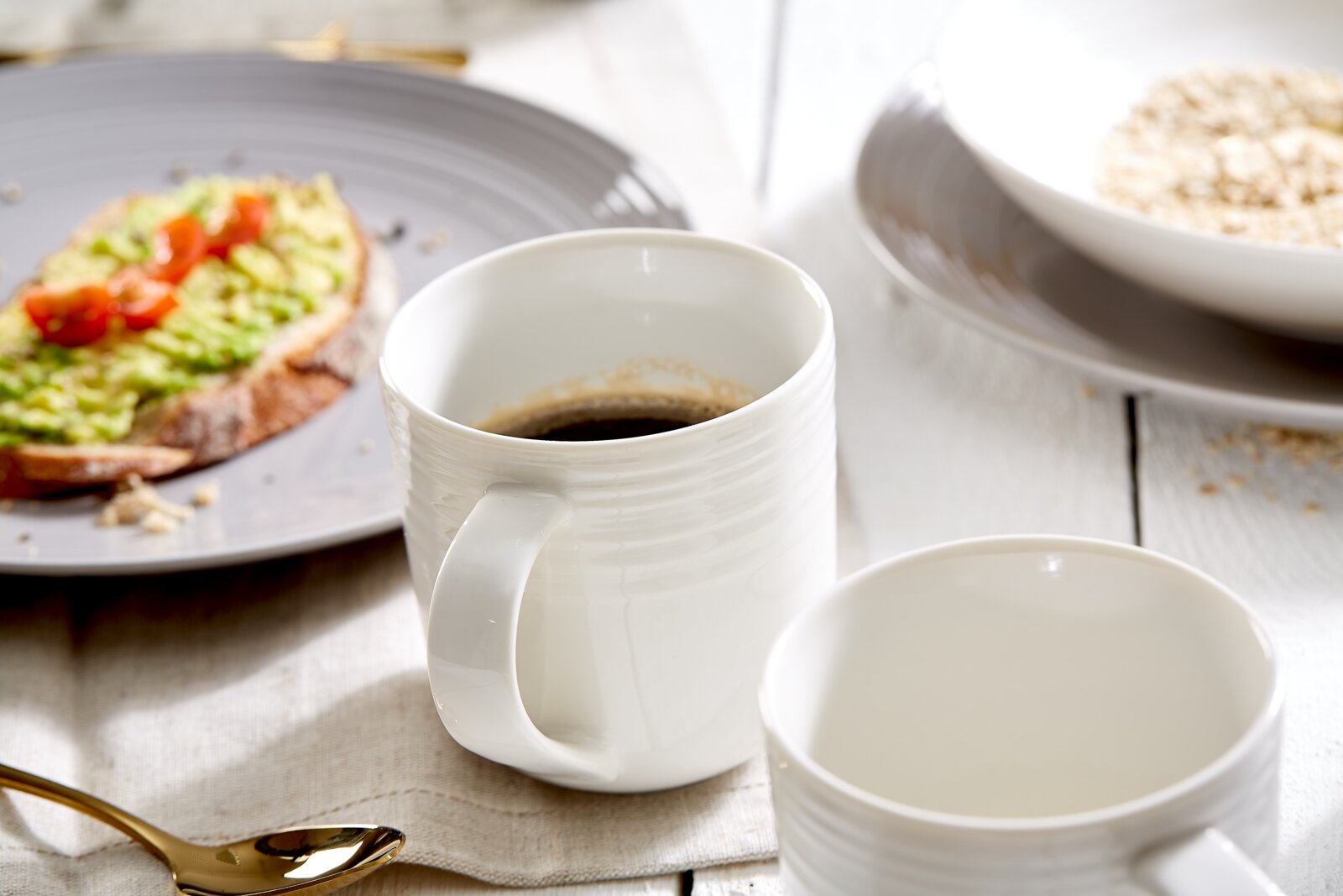 Weiße Kaffeetassen mit feiner Rillenstruktur in schräger Vorderansicht auf einem gedeckten Frühstückstisch