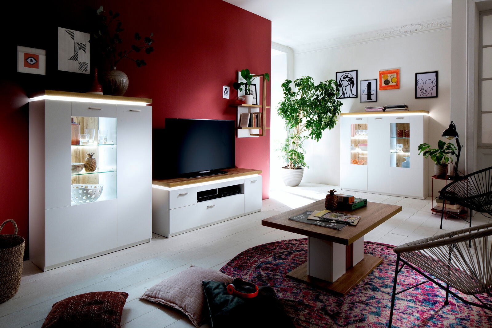 XORA Wohnkombination 2 CALI Moderne Wohnkombination mit weißem Schrank und TV-Möbel, dekoriert mit Pflanzen und Kunstwerken, aus der Perspektive des Wohnzimmers.