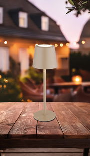 Moderne Tischleuchte in Beige auf einem Holztisch, fotografiert aus der Seitenperspektive mit einem unscharfen, stimmungsvollen Hintergrund.