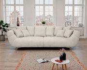 Helles, cremefarbenes Designer-Sofa mit vielen Kissen und schmalen Metallfüßen im modernen Wohnzimmer vor großen Fenstern, Frontalansicht.