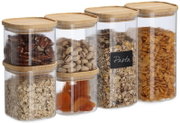 Set aus transparenten, geriffelten Vorratsdosen mit Bambusdeckeln, gefüllt mit Müsli, Nüssen und Cornflakes, in leicht schräger Frontansicht.