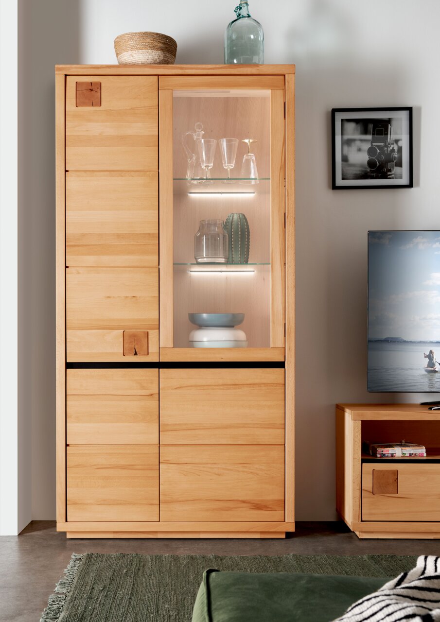 Houten vitrinekast met glazen deur en verlichting, gevuld met glazen en decoraties, gezien van voren.