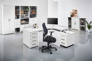 Moderne Büroumgebung mit weißem Eckschreibtisch, Rollcontainer und Bürostuhl, frontal betrachtet.