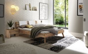 Modernes Schlafzimmer mit einem Kopfteil aus Holz und Metall, seitliche Perspektive. Das Bett ist mit neutralen Farben dekoriert und steht vor einer weißen Ziegelwand mit Kunstwerken.
