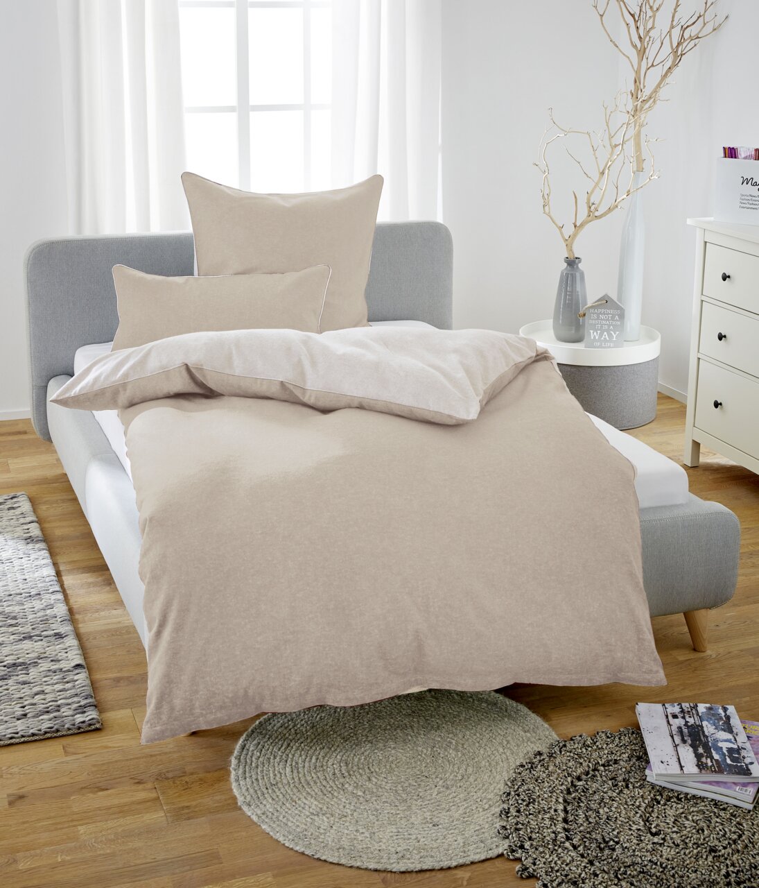 Beige Bettwäsche-Set aus Melange-Flanell auf einem grauen Bett, fotografiert aus einer frontalen Perspektive in einem hellen Schlafzimmer.