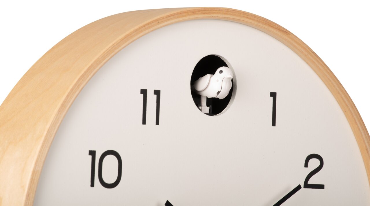 Nahaufnahme einer modernen Wanduhr mit hellem Holzrahmen und Kuckucksvogel, der aus einer Öffnung über der 12 herausschaut.