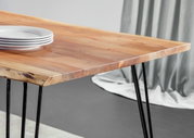 Nahaufnahme eines modernen Esstisches aus Holz mit Metallbeinen, von der Seite fotografiert. Auf dem Tisch liegen weiße Teller gestapelt.