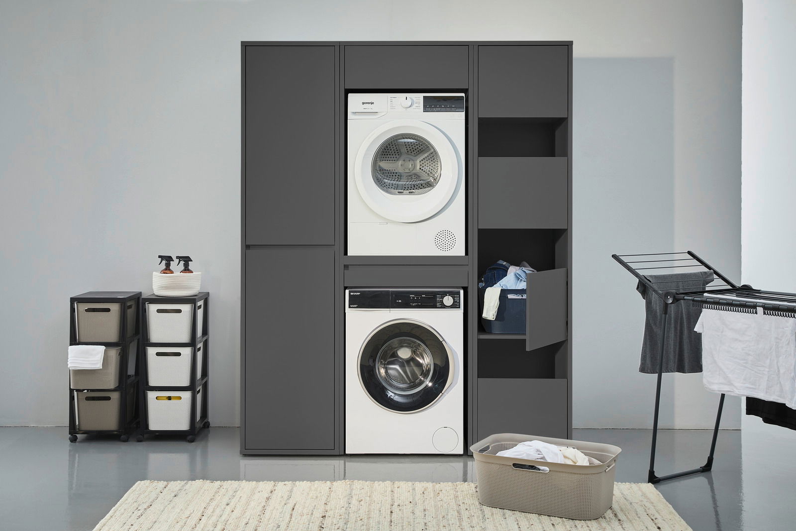 Waschmaschinenschrank in moderner Waschküche, frontal betrachtet, mit integriertem Trockner und Waschmaschine, sowie Stauraum für Wäsche und Reinigungsmittel.