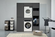 Waschmaschinenschrank in moderner Waschküche, frontal betrachtet, mit integriertem Trockner und Waschmaschine, sowie Stauraum für Wäsche und Reinigungsmittel.