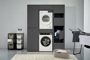 Waschmaschinenschrank in moderner Waschküche, frontal betrachtet, mit integriertem Trockner und Waschmaschine, sowie Stauraum für Wäsche und Reinigungsmittel.