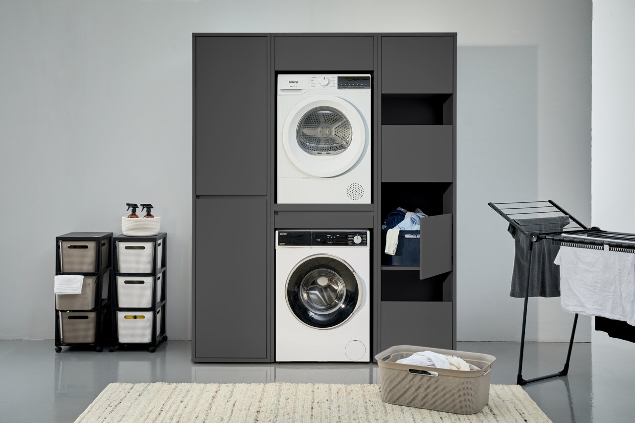 Waschmaschinenschrank in moderner Waschküche, frontal betrachtet, mit integriertem Trockner und Waschmaschine, sowie Stauraum für Wäsche und Reinigungsmittel.
