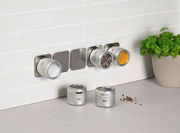 Gewürzdosenset an der Wand montiert, mit drei Dosen gefüllt mit Salz, Pfeffer und Kurkuma, und zwei Dosen auf der Arbeitsfläche. Perspektive von vorne.