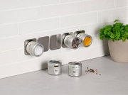 Gewürzdosenset an der Wand montiert, mit drei Dosen gefüllt mit Salz, Pfeffer und Kurkuma, und zwei Dosen auf der Arbeitsfläche. Perspektive von vorne.