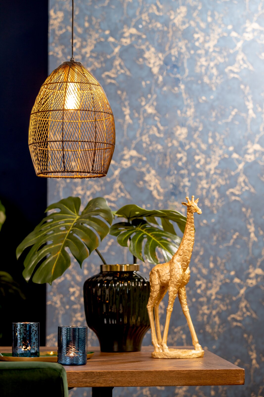Light&Living Hängeleuchte MEYA Goldene Giraffen-Dekoskulptur in leichter Dreiviertelansicht auf einem Holztisch, stilvoll inszeniert mit Monstera, schwarzer Vase und warm leuchtender Pendelleuchte