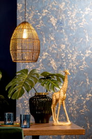 Goldene Giraffen-Dekoskulptur in leichter Dreiviertelansicht auf einem Holztisch, stilvoll inszeniert mit Monstera, schwarzer Vase und warm leuchtender Pendelleuchte