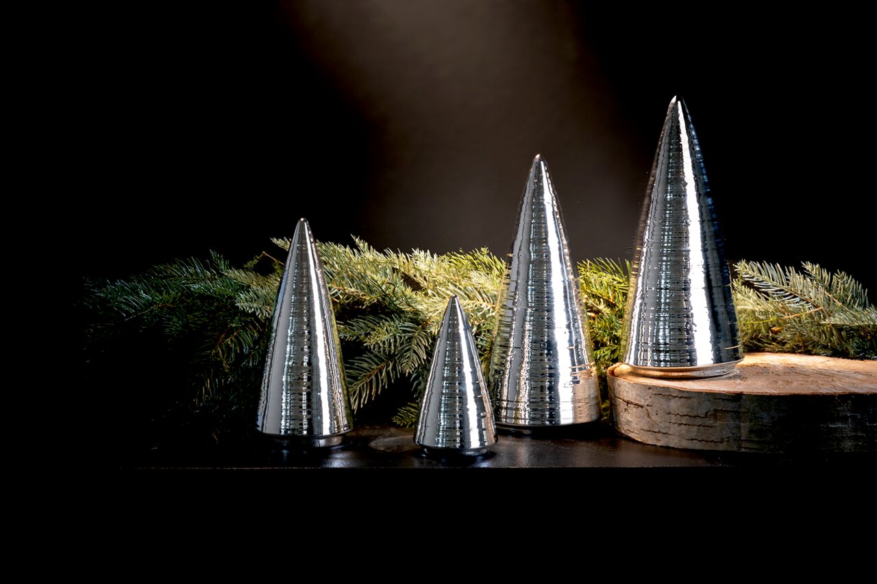 Zilveren decoratieve bomen in kegelvorm, in verschillende maten, op een tafel met dennentakken en een houten schijf, zijaanzicht.