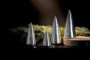 Zilveren decoratieve bomen in kegelvorm, in verschillende maten, op een tafel met dennentakken en een houten schijf, zijaanzicht.