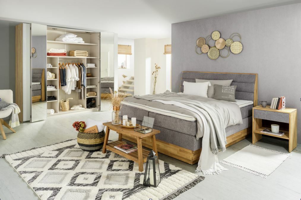 Gemütliches Schlafzimmer mit Boxspringbett MARISSA in Holzoptik, grauem Polster und passender Nachtkommode, aus der Perspektive von vorne rechts.