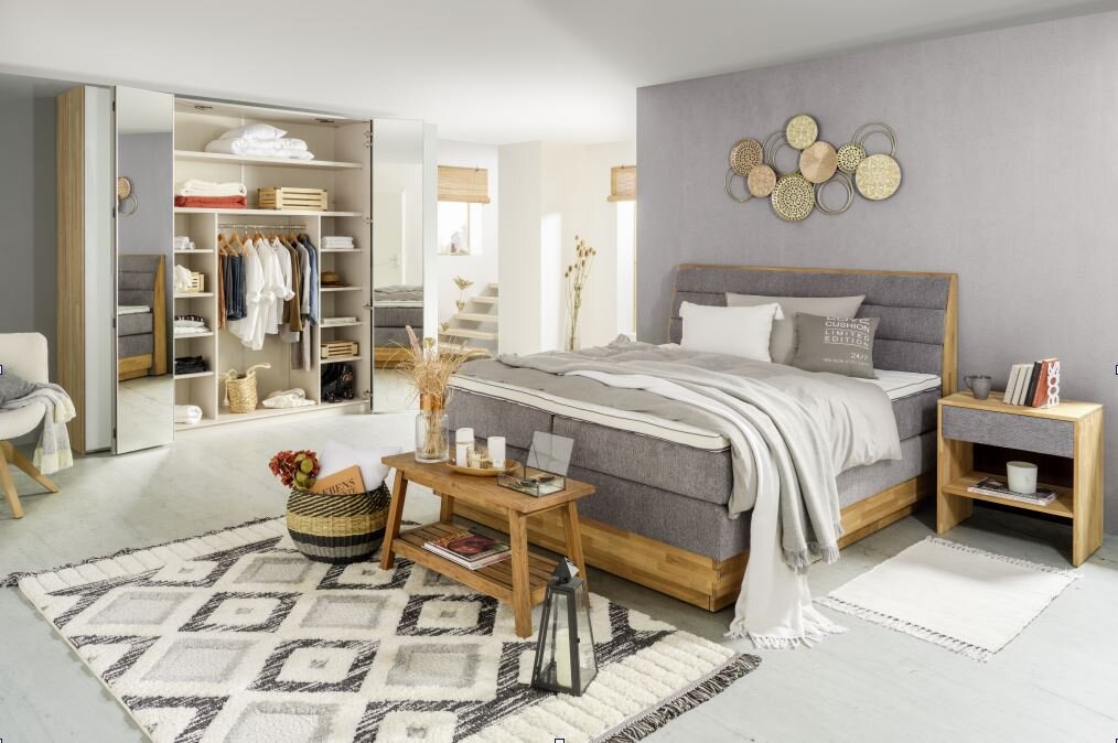 Gemütliches Schlafzimmer mit Boxspringbett MARISSA in Holzoptik, grauem Polster und passender Nachtkommode, aus der Perspektive von vorne rechts.