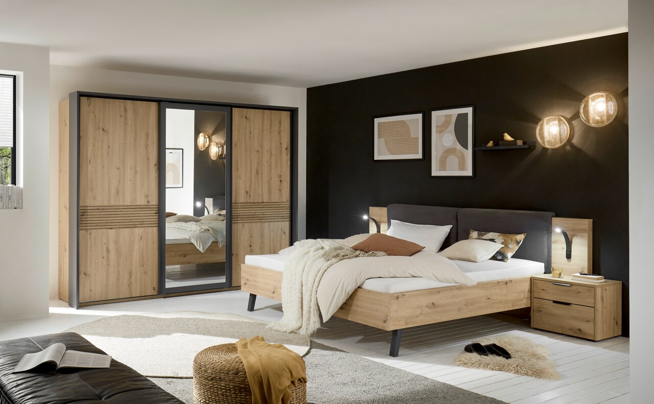 Moderner Schwebetürenschrank mit drei Türen, davon eine mit Spiegel, in einem stilvollen Schlafzimmer mit Holzbett und Nachttisch. Perspektive: Frontalansicht des Schranks.