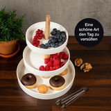 Dreistufige weiße Etagere mit Holzgriff, gefüllt mit Beeren und Gebäck, von oben fotografiert.