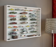 Weiße, wandmontierte Glasvitrine mit mehreren Glasböden und Schiebetüren, gefüllt mit Modellautos und kleinen Sammlerstücken; Frontansicht in leichter Perspektive von rechts.