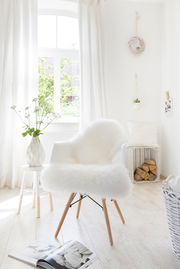 Weißes Schaffell auf einem modernen Stuhl in einem hellen, gemütlichen Raum mit Holzfußboden und natürlichem Licht von einem Fenster.