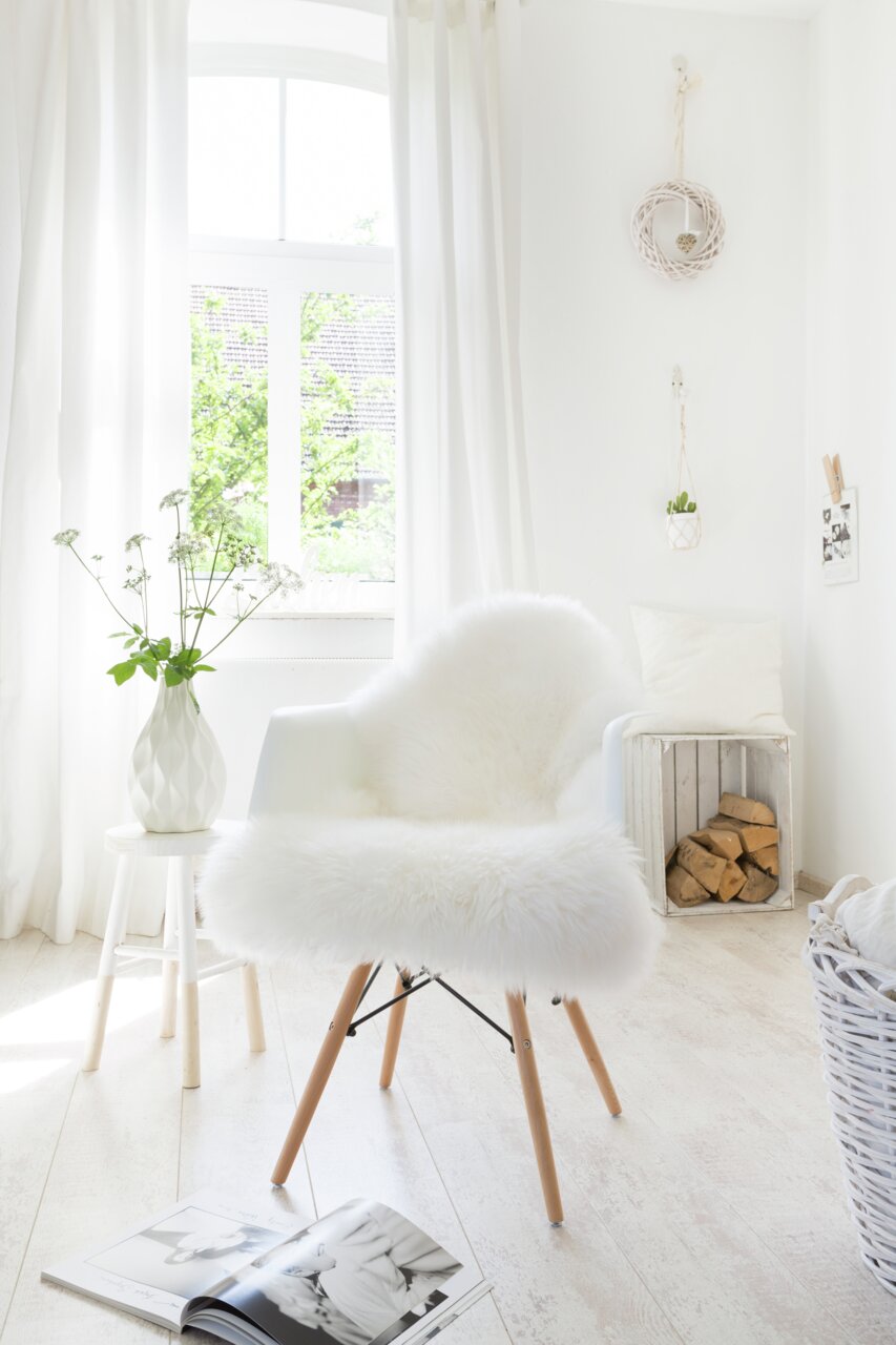 Zurbrüggen Schaffell ca. 85cm Weißes Schaffell auf einem modernen Stuhl in einem hellen, gemütlichen Raum mit Holzfußboden und natürlichem Licht von einem Fenster.