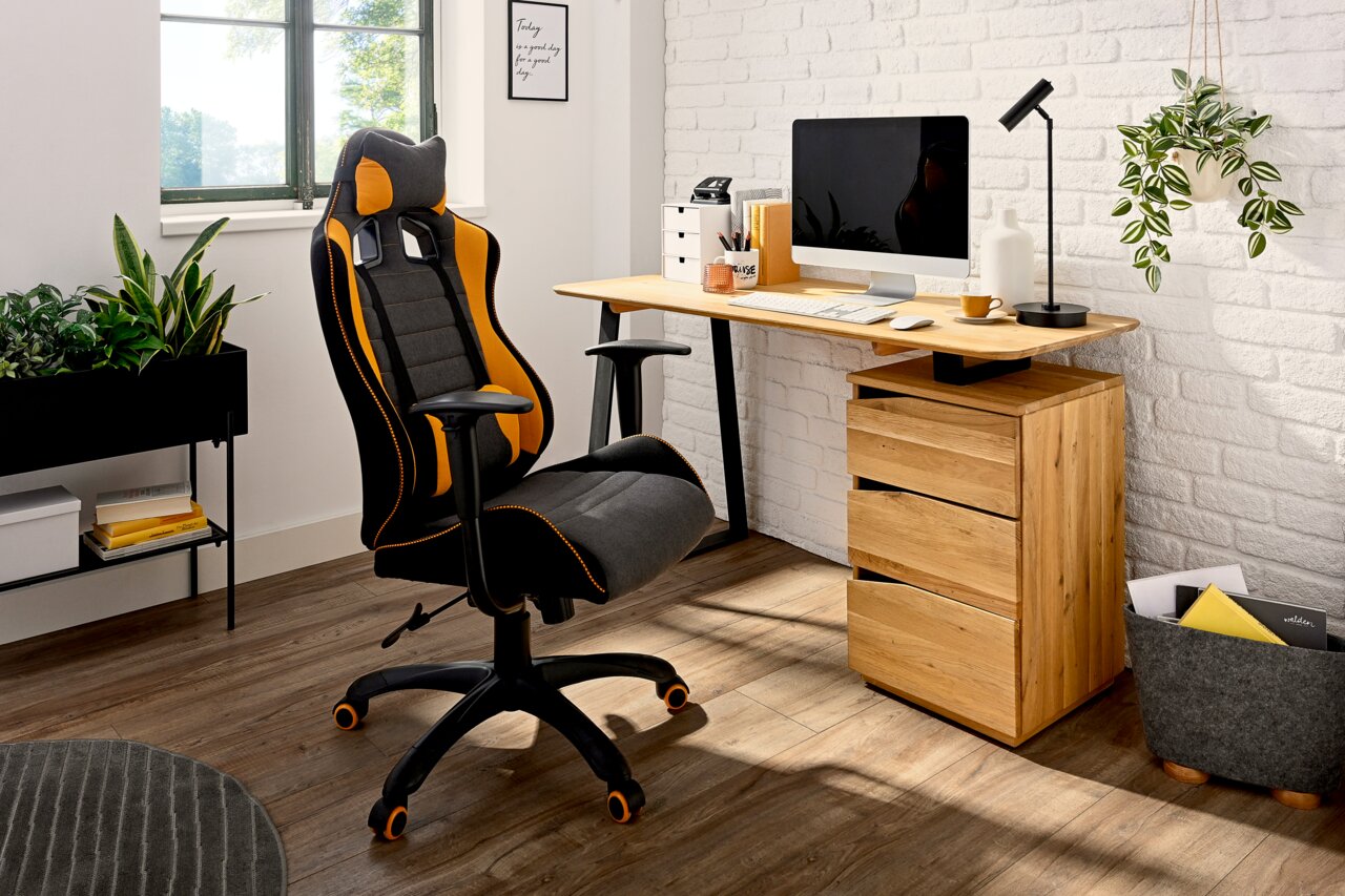 Modern houten bureau met lades, gezien vanaf de zijkant, naast een ergonomische bureaustoel in een lichte ruimte.