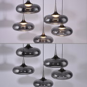 Mehrere moderne Pendelleuchten mit rauchgrauen, ovalen Glasschirmen und dunklen Metallspitzen, warm leuchtend, in leichter Untersicht vor hellem Hintergrund