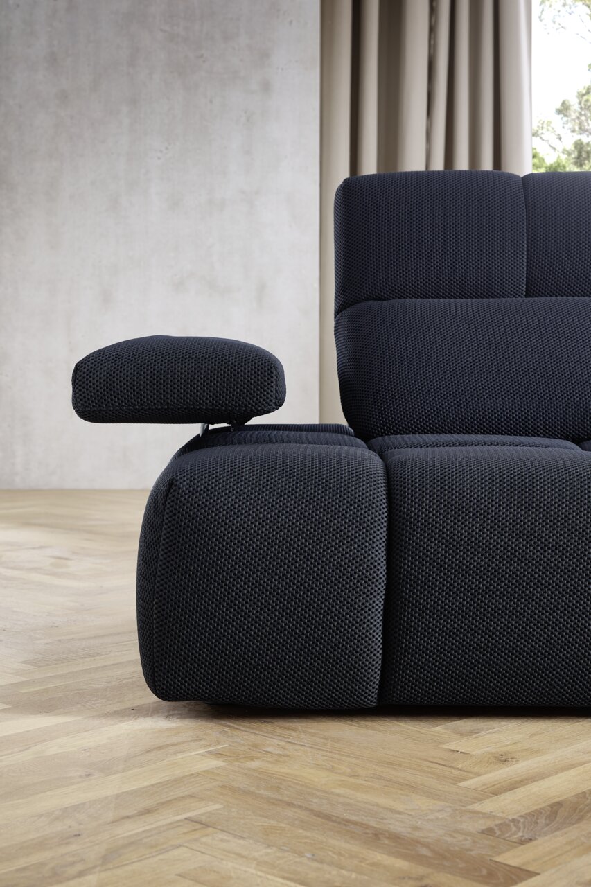 Nahaufnahme einer modernen, dunkelblauen Eckgarnitur mit verstellbarer Armlehne, seitliche Perspektive.