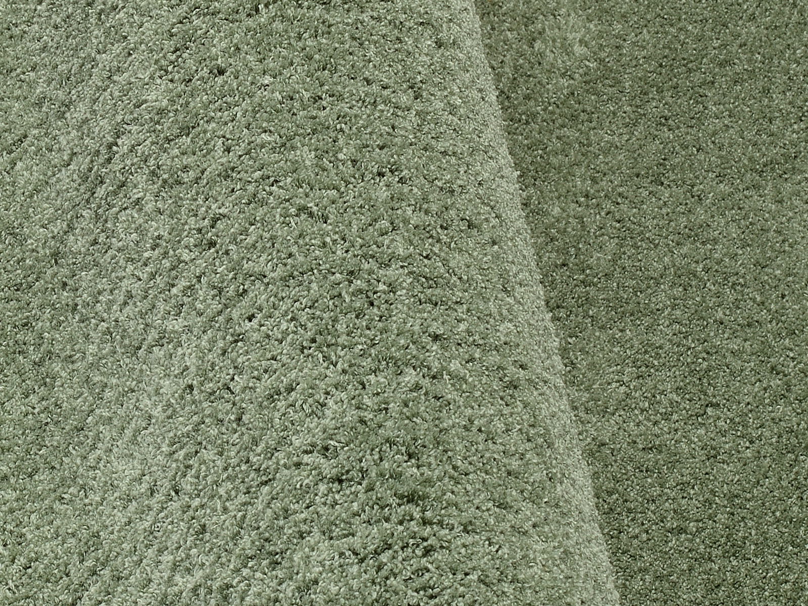 Nahaufnahme eines weichen, grünen Teppichs mit flauschiger Textur, perspektivisch von der Seite aufgenommen.