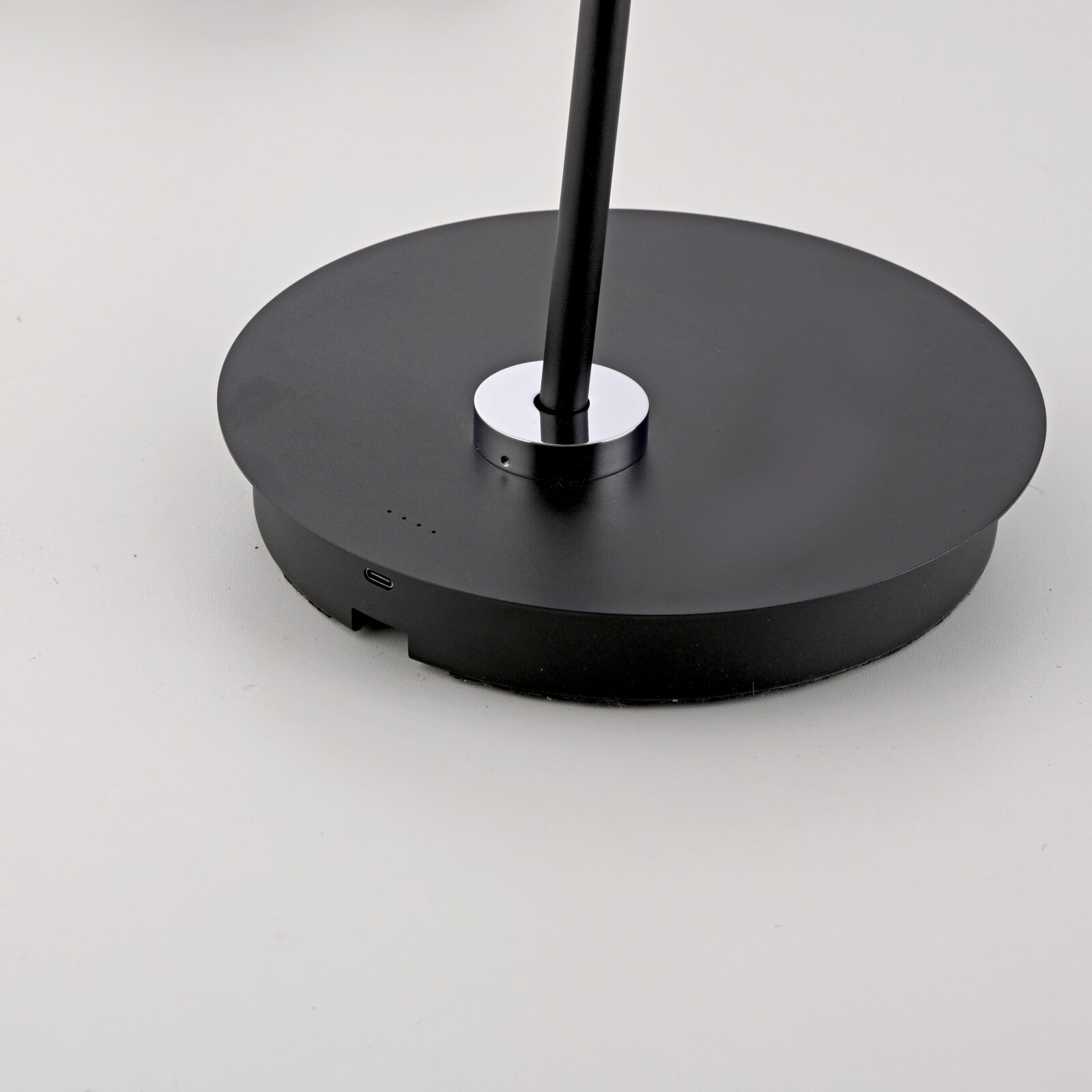 Close-up van de voet van een zwarte staande lamp op accu met USB-aansluiting en laadindicator.