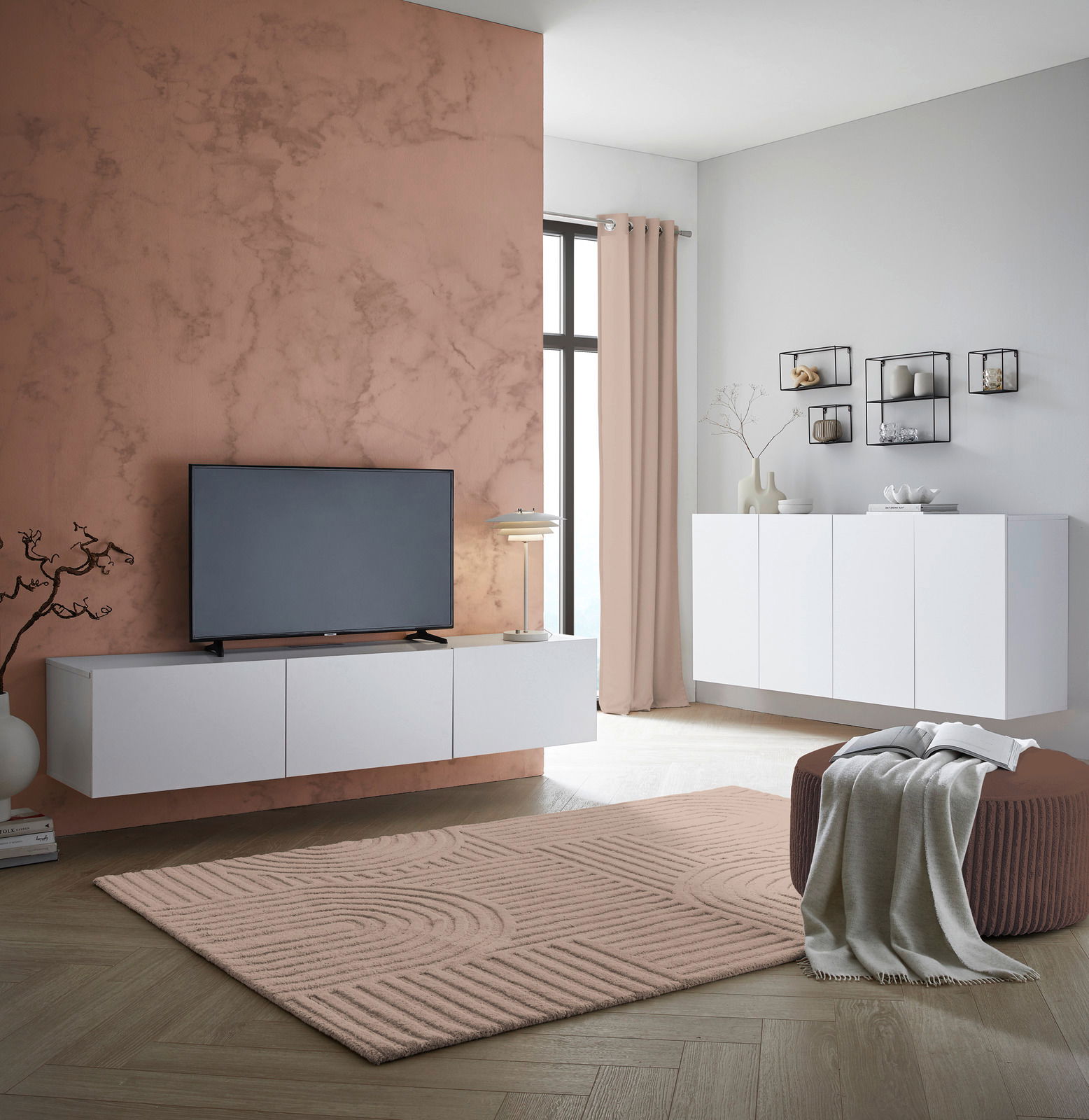 Modernes TV-Hängelowboard in Weiß, frontal betrachtet, montiert an einer Wand mit Marmoroptik, neben einem großen Fenster.