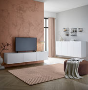 Modernes TV-Hängelowboard in Weiß, frontal betrachtet, montiert an einer Wand mit Marmoroptik, neben einem großen Fenster.