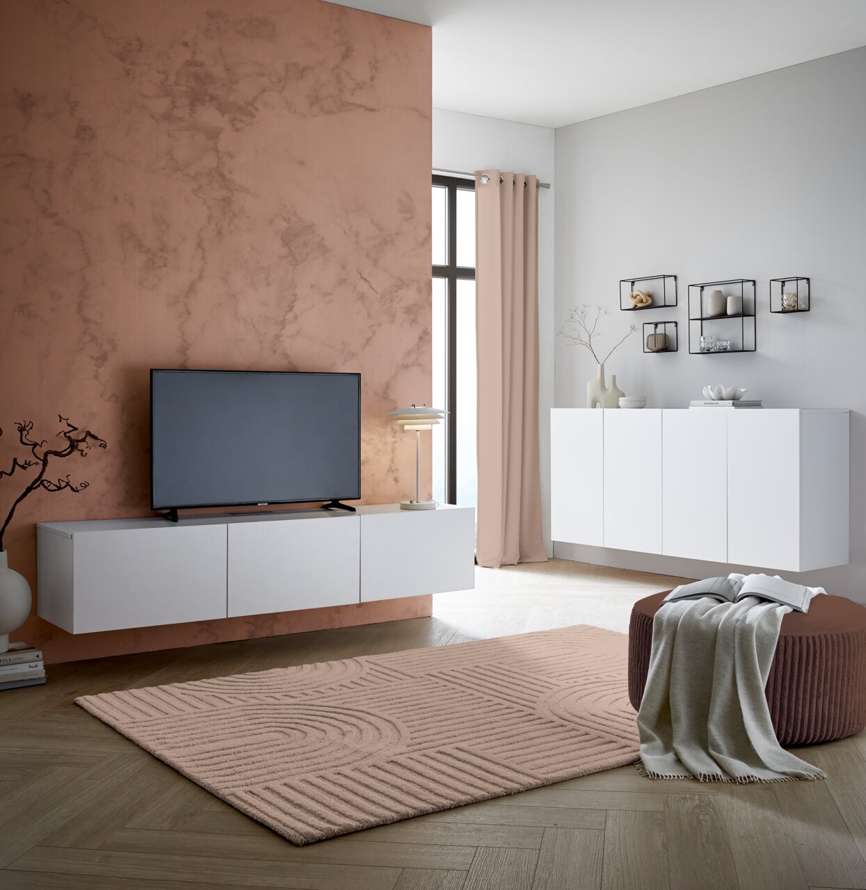 Modernes TV-Hängelowboard in Weiß, frontal betrachtet, montiert an einer Wand mit Marmoroptik, neben einem großen Fenster.