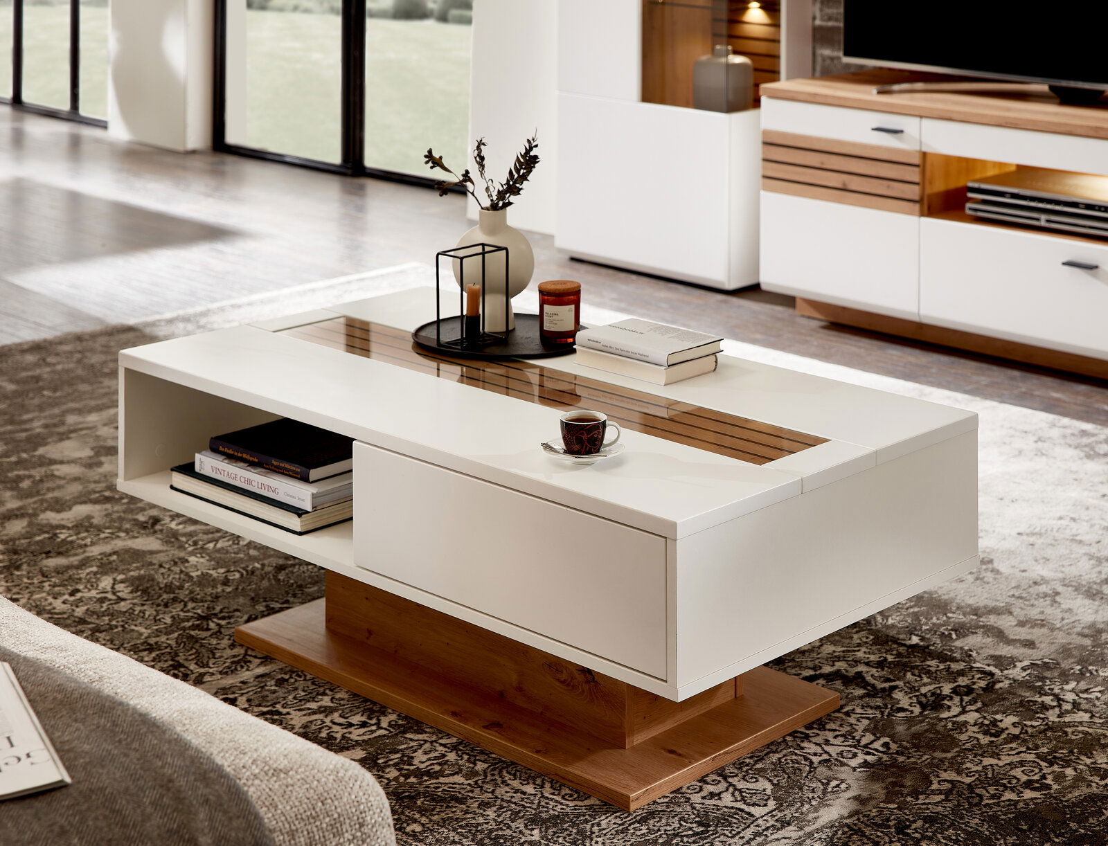 Moderner Couchtisch in Weiß mit Holzdetails, dekoriert mit Büchern und einer Tasse, seitliche Perspektive