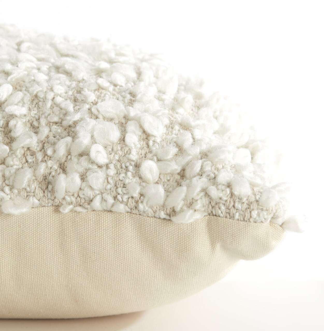 Nahaufnahme eines Kissens mit bouclé Textur in Cremeweiß, seitliche Perspektive