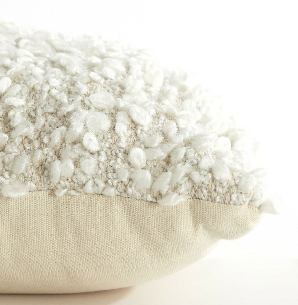 Nahaufnahme eines Kissens mit bouclé Textur in Cremeweiß, seitliche Perspektive