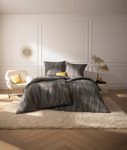 Blick auf ein stilvoll eingerichtetes Schlafzimmer mit Estella Bettwäsche CAJA in Grau und Gelb auf einem Bett, umgeben von eleganter Dekoration.