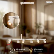 Weiße, längliche Pendelleuchte mit sechs schwenkbaren Spot-Strahlern an einer geraden Leiste, warmweiß leuchtend, an zwei schwarzen Kabeln von der Decke hängend, Produktansicht von vorne mit leichtem Untersichtwinkel.