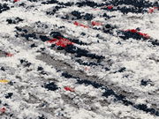 Nahaufnahme eines Designer Teppichs mit abstraktem Muster in Weiß, Grau, Blau und Rot.