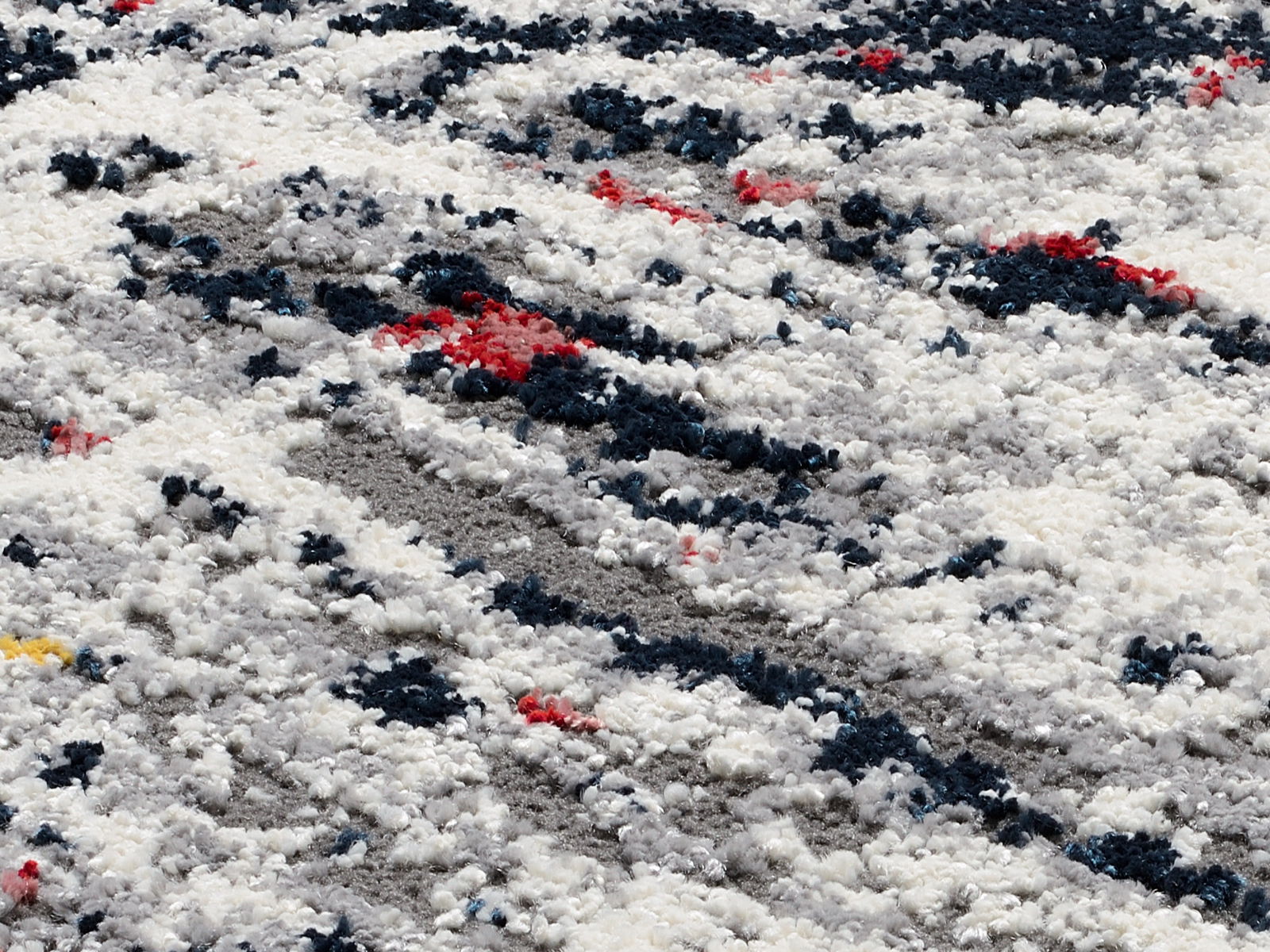 Nahaufnahme eines Designer Teppichs mit abstraktem Muster in Weiß, Grau, Blau und Rot.