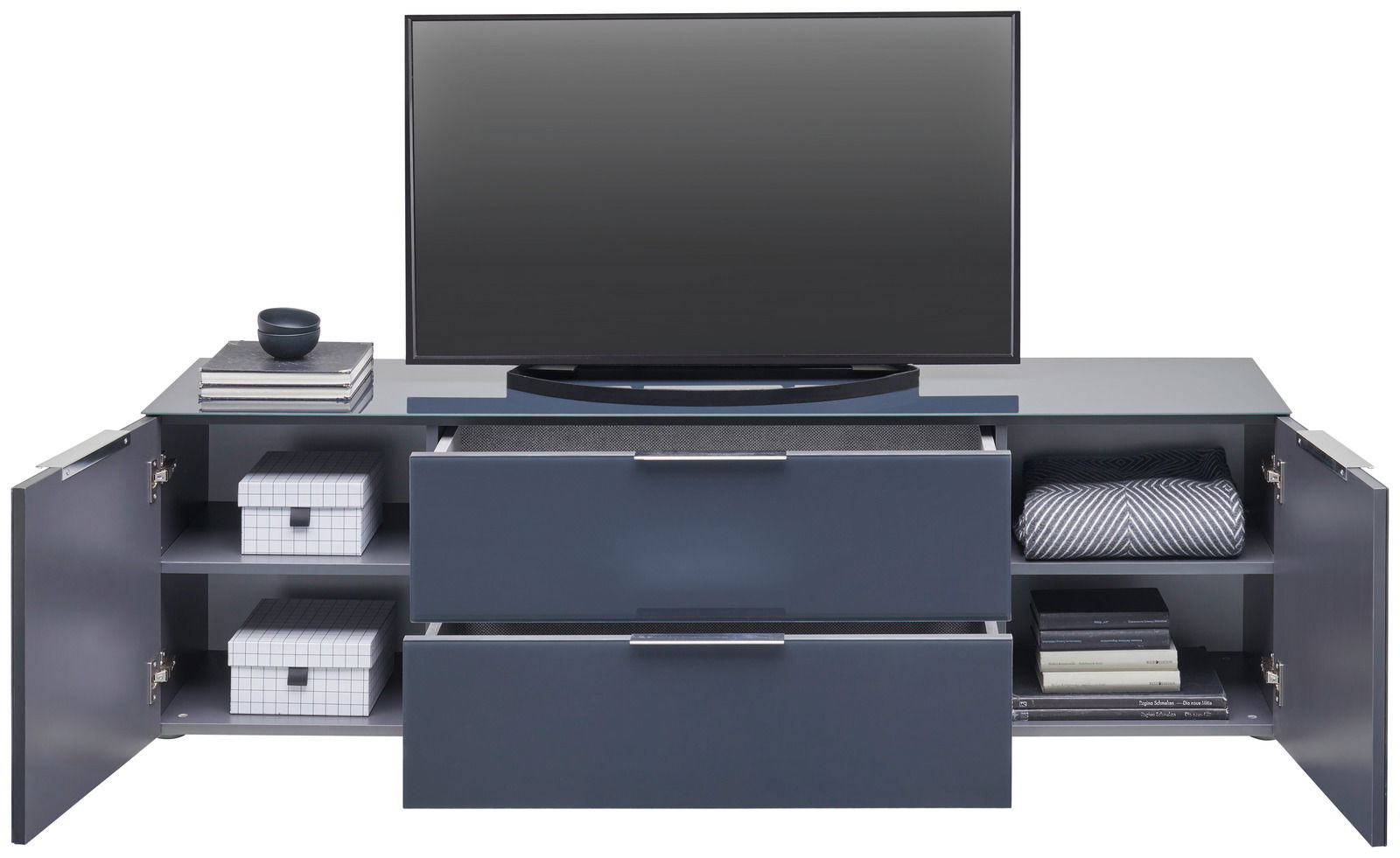 Frontale Ansicht eines modernen TV-Lowboards mit zwei Schubladen und seitlichen Fächern, dekoriert mit Büchern, Boxen und einer Decke.