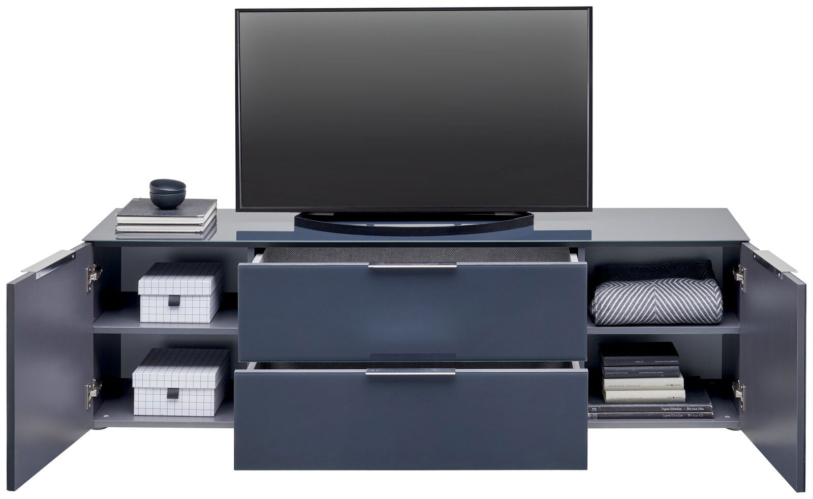 Frontale Ansicht eines modernen TV-Lowboards mit zwei Schubladen und seitlichen Fächern, dekoriert mit Büchern, Boxen und einer Decke.