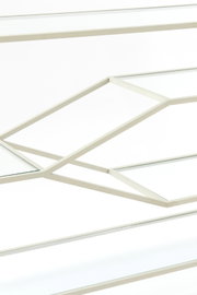 Nahaufnahme eines Konsolentisches mit geometrischem Metallrahmen und Glasplatten, seitliche Perspektive