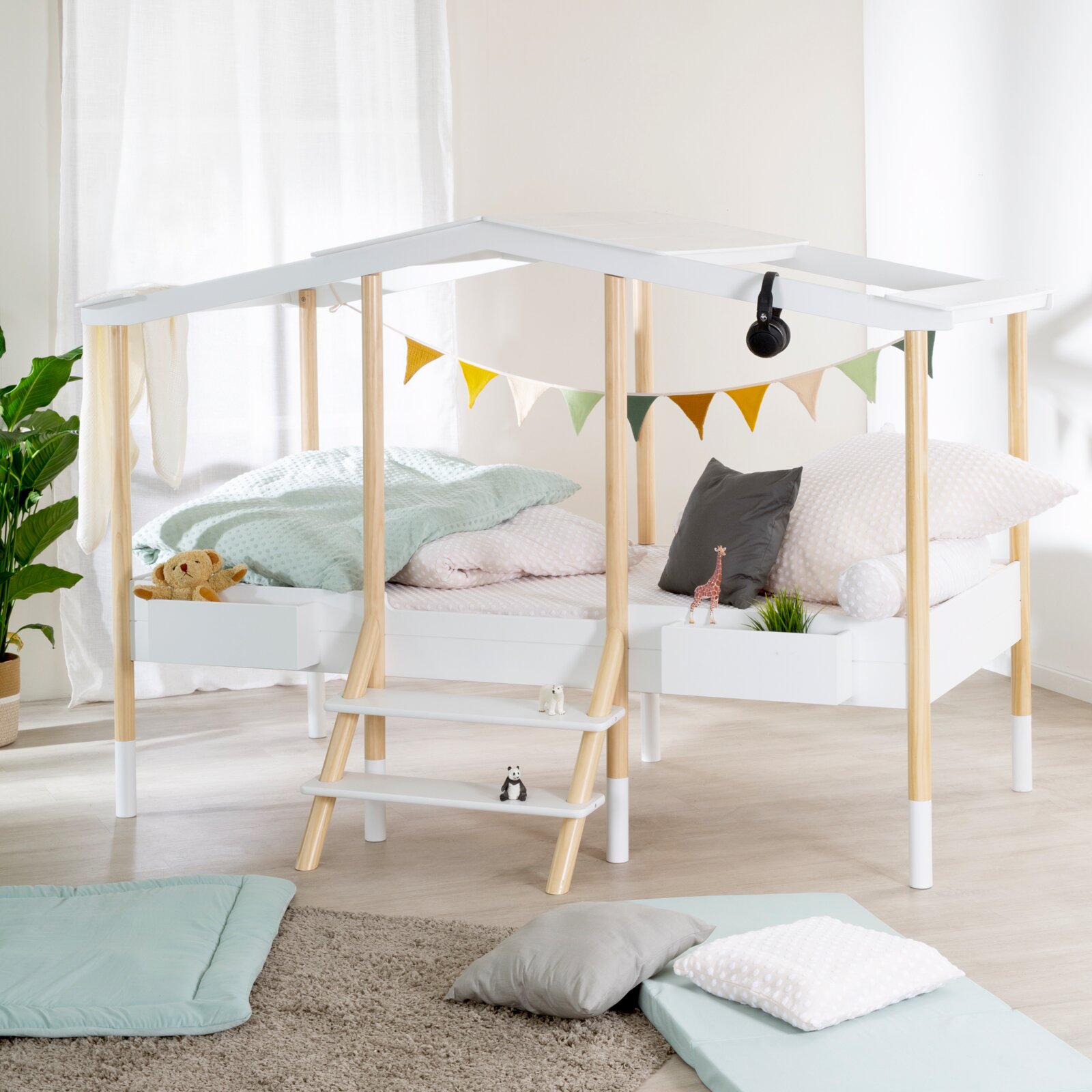 Kinder-Hochbett in Hausform aus weißem Holz und Naturholz mit Leiter, Ablagen und gemütlicher Bettwäsche, aus schräger Vorderansicht