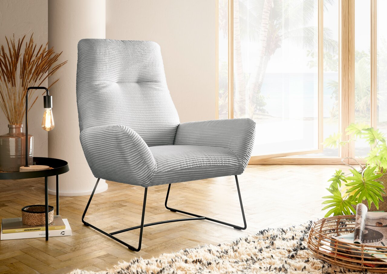 Moderner grauer Sessel mit geripptem Stoffbezug, seitliche Perspektive, in einem hellen Raum mit großen Fenstern und Holzboden.