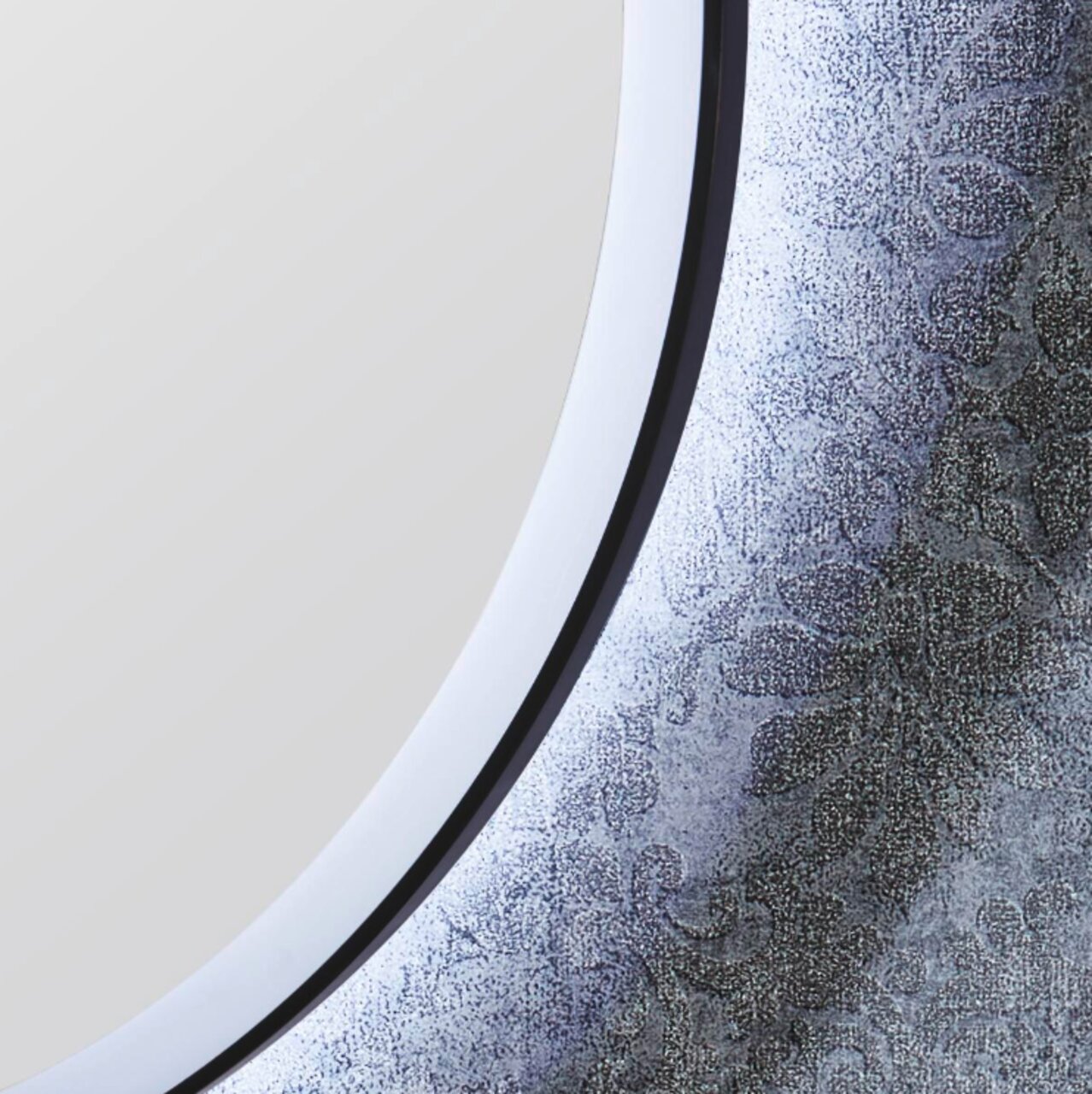 Close-up van een ronde spiegel met een decoratieve lijst met bloemmotief, gezien vanaf de zijkant