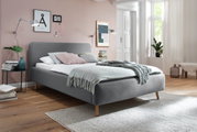 Graues Polsterbett in einem modernen Schlafzimmer mit Holzfußboden, dekoriert mit Kissen und Decken, seitliche Perspektive.